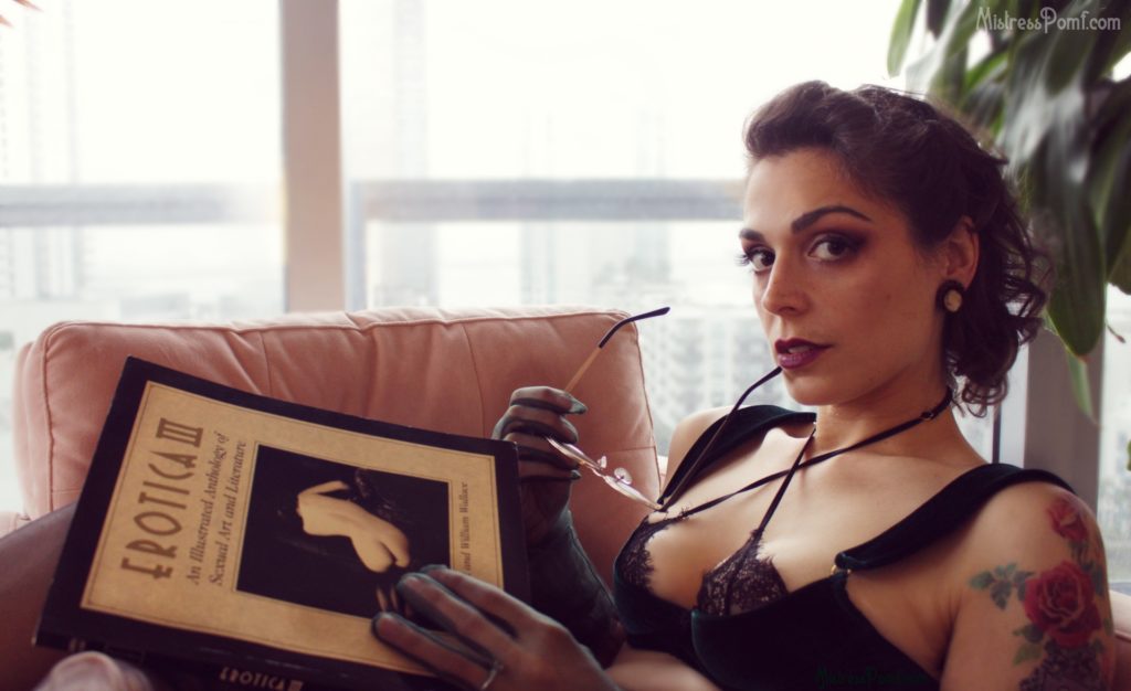 Dominatrix Mistress Pomf embodies BDSM roleplay fetish as she holds her sexy librarian glasses up to her lips and looks at you from afar while reading an erotica book from her BDSM fetish library.