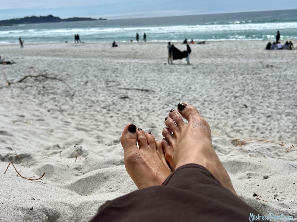 Pictured are Dominatrix Mistress Pomf's gorgeous sandy feet at the beach. Her toenails are painted a dark copper color.